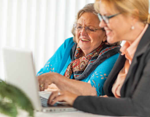 woman helping senior adult lady on laptop computer